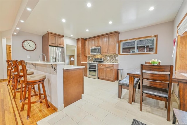 kitchen with light countertops, appliances with stainless steel finishes, decorative backsplash, and brown cabinets