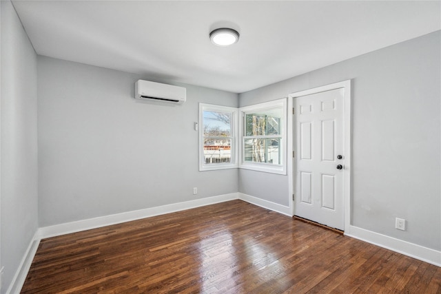 unfurnished room with a wall unit AC, baseboards, and wood finished floors