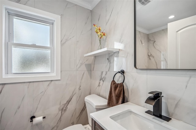 half bathroom featuring visible vents, toilet, ornamental molding, vanity, and tile walls