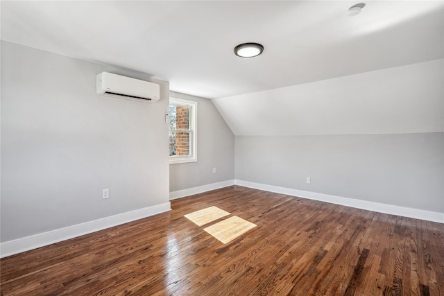 additional living space featuring lofted ceiling, an AC wall unit, hardwood / wood-style flooring, and baseboards