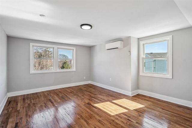 unfurnished room featuring an AC wall unit, hardwood / wood-style floors, a wealth of natural light, and baseboards