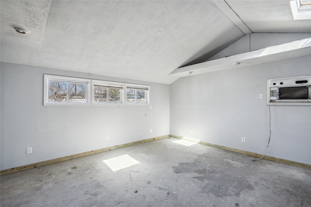 unfurnished room featuring lofted ceiling, unfinished concrete flooring, and baseboards