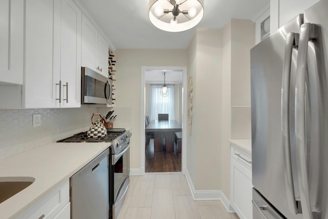 kitchen with backsplash, appliances with stainless steel finishes, white cabinetry, a chandelier, and baseboards