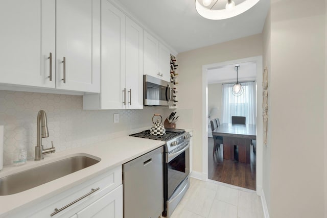 kitchen with stainless steel appliances, a sink, white cabinets, light countertops, and tasteful backsplash