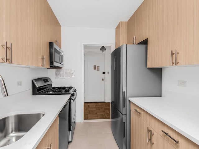 kitchen with appliances with stainless steel finishes, light countertops, a sink, and light brown cabinetry