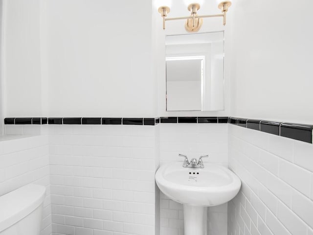 half bathroom featuring wainscoting, tile walls, and toilet