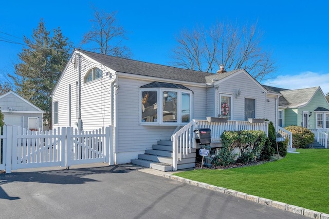 bungalow-style house featuring a shingled roof, fence, a deck, an outdoor structure, and a front yard