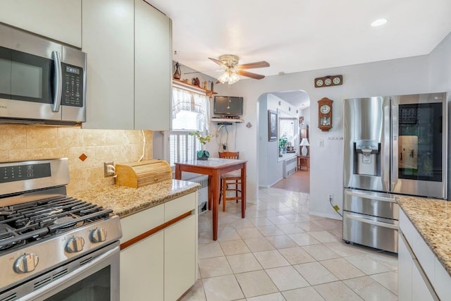 kitchen featuring light tile patterned floors, arched walkways, decorative backsplash, a ceiling fan, and stainless steel appliances