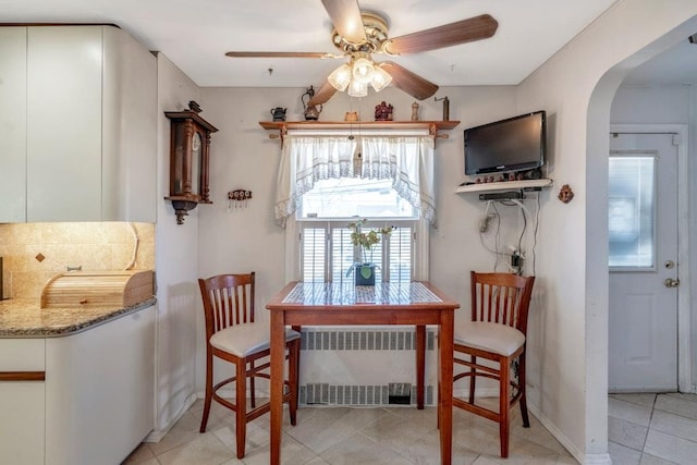 dining area with arched walkways, light tile patterned floors, a ceiling fan, baseboards, and radiator heating unit