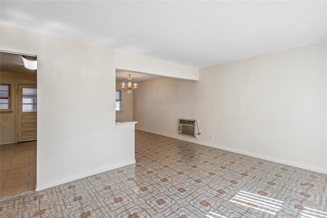 empty room featuring a wall unit AC, a notable chandelier, and baseboards