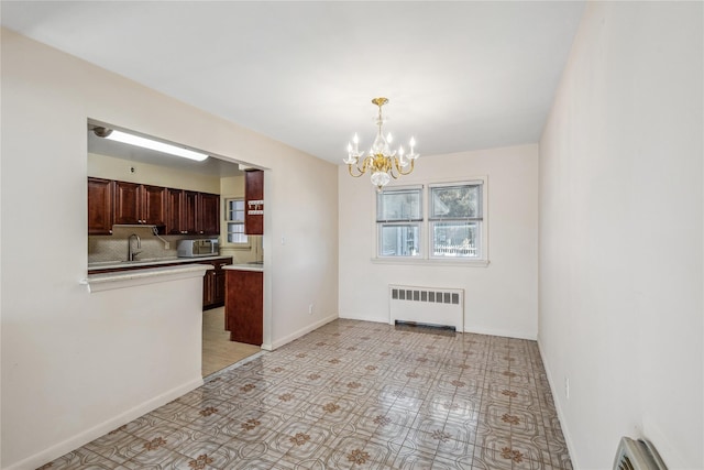 unfurnished dining area with a notable chandelier, baseboard heating, radiator heating unit, a sink, and baseboards