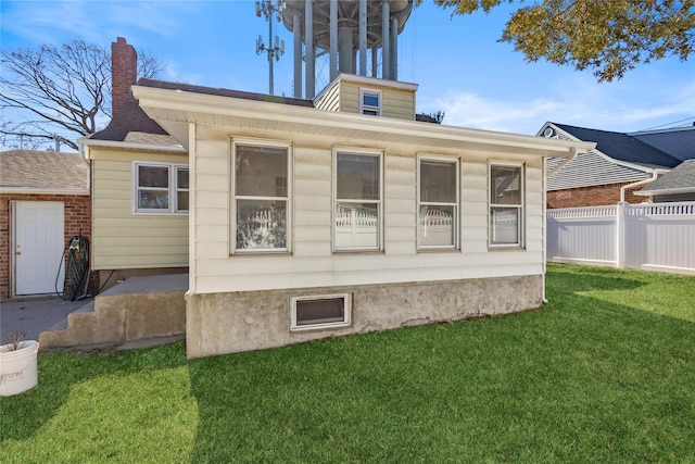 back of property featuring a chimney, fence, and a lawn