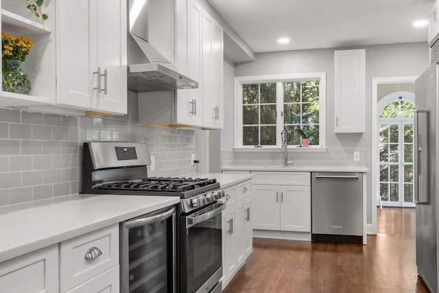 kitchen with stainless steel appliances, wall chimney range hood, white cabinetry, open shelves, and a sink