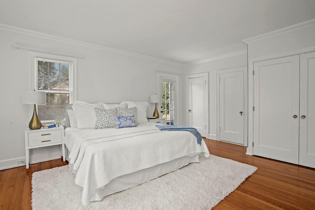 bedroom featuring ornamental molding, wood finished floors, multiple windows, and two closets