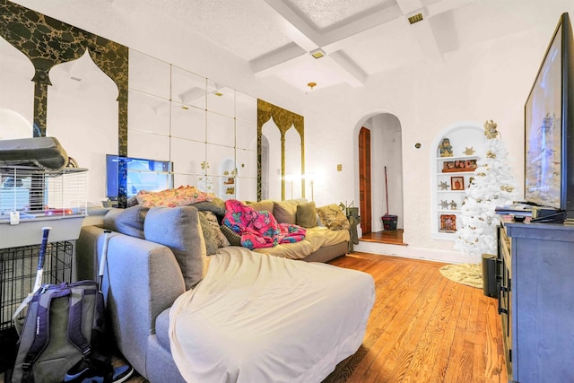 living area featuring arched walkways, coffered ceiling, built in features, beam ceiling, and hardwood / wood-style floors