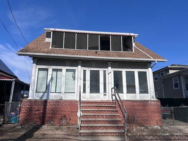 view of front of house featuring brick siding, fence, a sunroom, roof with shingles, and a gate