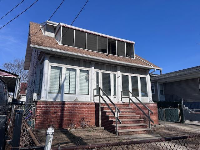 view of front of house featuring a sunroom, a shingled roof, fence, and brick siding