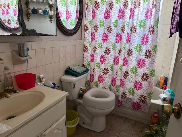 bathroom with toilet, shower / tub combo, vanity, tile walls, and tile patterned floors