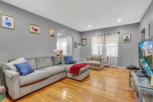 living room with arched walkways, light wood-style flooring, and baseboards