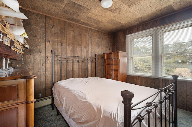 bedroom featuring baseboard heating, dark carpet, and wooden walls