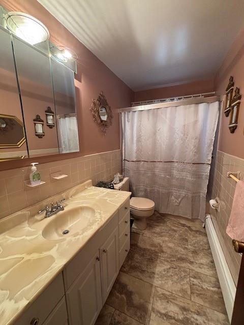 full bath featuring toilet, a shower with shower curtain, vanity, tile walls, and wainscoting