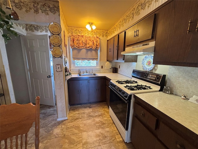 kitchen featuring light countertops, a sink, white gas range oven, under cabinet range hood, and wallpapered walls