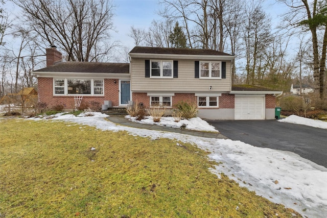 tri-level home with a yard, brick siding, driveway, and a chimney