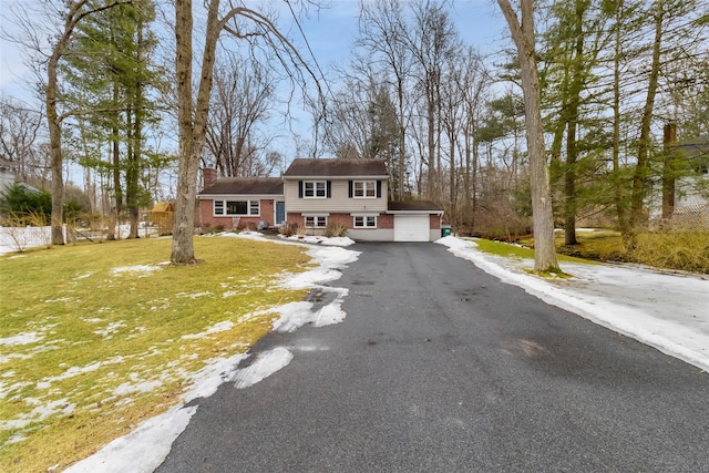 view of front facade with aphalt driveway, a garage, brick siding, a chimney, and a front yard