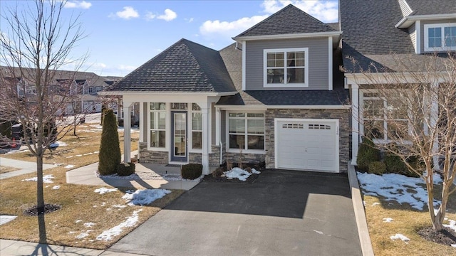 view of front of property featuring driveway, stone siding, a shingled roof, and a garage