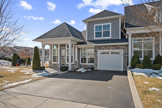 view of front of house with driveway, stone siding, a garage, and roof with shingles