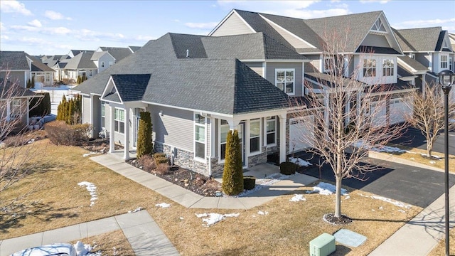 view of front of house featuring a front yard, stone siding, a residential view, and roof with shingles