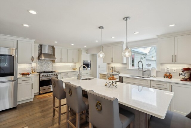 kitchen with a sink, a kitchen breakfast bar, appliances with stainless steel finishes, and wall chimney exhaust hood