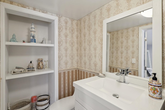 half bathroom with toilet, wallpapered walls, and vanity