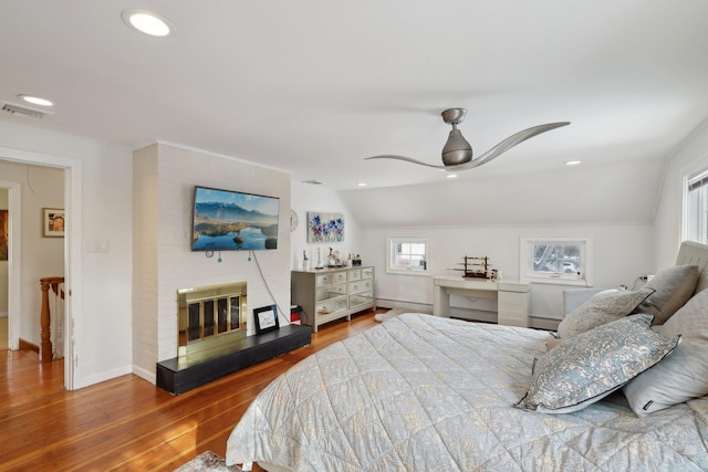 bedroom with a glass covered fireplace, wood finished floors, recessed lighting, lofted ceiling, and ceiling fan