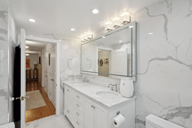 bathroom featuring toilet, double vanity, recessed lighting, tile walls, and a sink