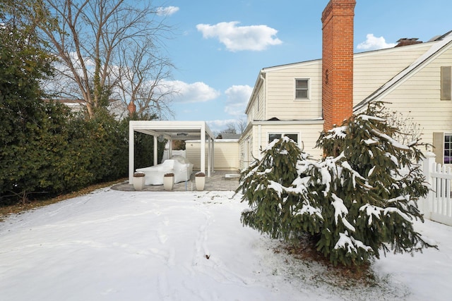 snow covered rear of property with a carport and a chimney