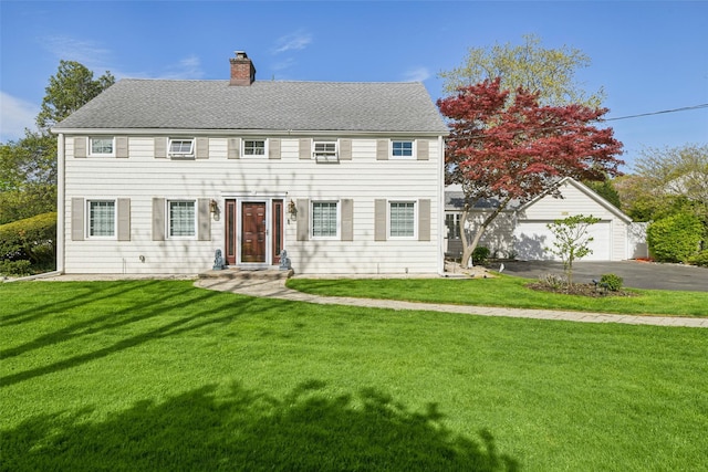 colonial-style house featuring a shingled roof, a front lawn, driveway, and a chimney