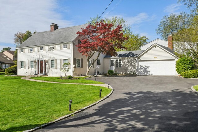 colonial house with a garage, a chimney, a front lawn, and aphalt driveway