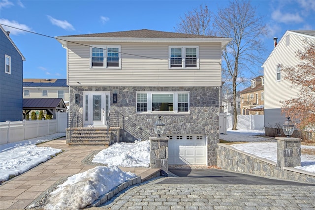 view of front of property with a garage, stone siding, fence, and decorative driveway