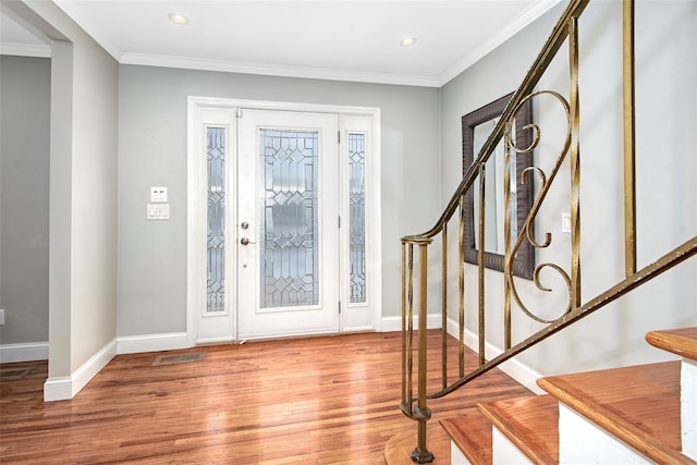 entryway with wood finished floors, visible vents, baseboards, ornamental molding, and stairway