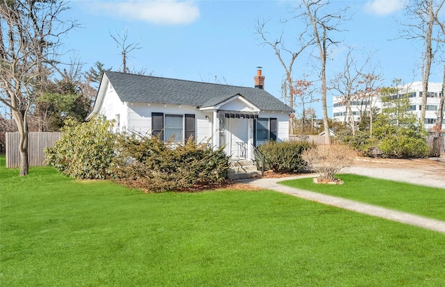 view of front facade featuring driveway, a shingled roof, a chimney, fence, and a front yard