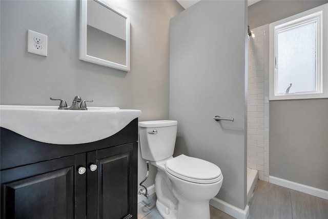 full bathroom with toilet, wood finished floors, vanity, baseboards, and tiled shower