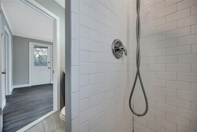 bathroom with toilet, baseboards, tiled shower, and wood finished floors