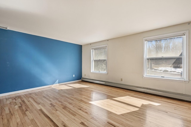 spare room with a baseboard radiator, visible vents, baseboards, and wood finished floors