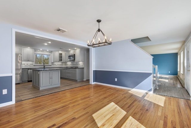 kitchen featuring light wood finished floors, tasteful backsplash, dark countertops, appliances with stainless steel finishes, and gray cabinets