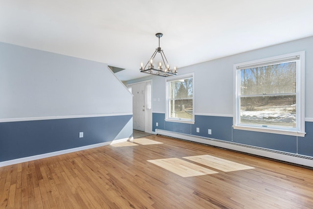 unfurnished dining area featuring a chandelier, a baseboard radiator, wood-type flooring, and baseboards