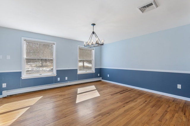 empty room with visible vents, baseboard heating, wood finished floors, and a chandelier