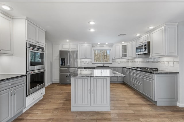 kitchen featuring visible vents, dark stone counters, a kitchen island, appliances with stainless steel finishes, and a sink