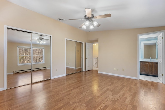 unfurnished bedroom with light wood finished floors, two closets, visible vents, a baseboard heating unit, and baseboards