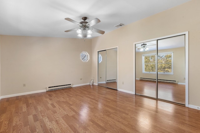 unfurnished bedroom with multiple closets, a baseboard radiator, visible vents, a baseboard heating unit, and wood finished floors